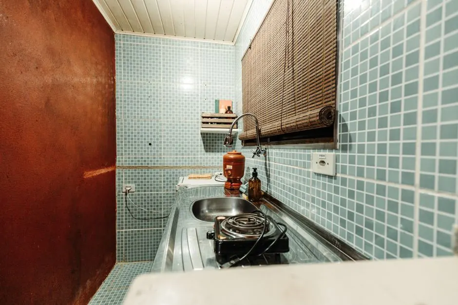 A cozy kitchenette with blue tiles, sink, and a single electric burner.