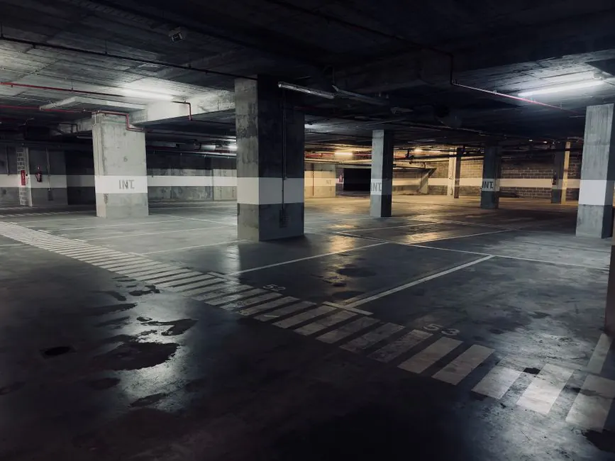 A moody underground parking garage featuring empty spaces and puddles on the floor.