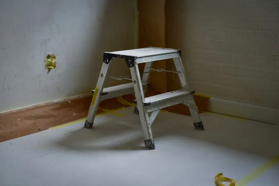 A sturdy metal ladder placed on a taped-off floor in a room under renovation.