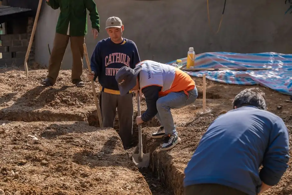 Volunteers working together to dig a trench at a construction site in daylight.